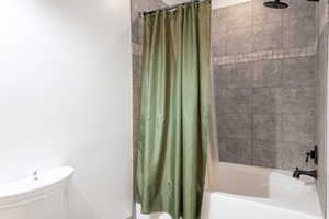 Full bathroom featuring shower / bathtub combination with curtain and toilet