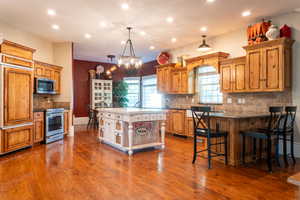 Kitchen featuring appliances with stainless steel finishes, tasteful backsplash, recessed lighting, brown cabinets, and a breakfast bar