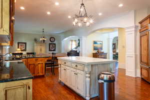 Kitchen featuring arched walkways, dark wood-type flooring, ornamental molding, a sink, and ornate columns