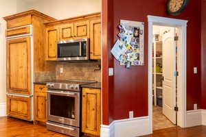 Kitchen featuring stainless steel appliances, dark countertops, brown cabinets, decorative backsplash, and light wood finished floors