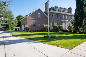 Colonial inspired home with brick siding, a front yard, concrete driveway, and a chimney