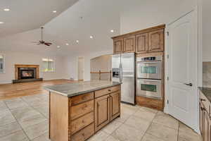 Kitchen featuring stainless steel appliances, a ceiling fan, light tile patterned floors, a glass covered fireplace, and recessed lighting