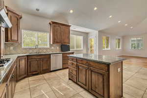 Kitchen with a sink, appliances with stainless steel finishes, backsplash, range hood, and light tile patterned flooring