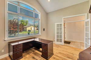 Unfurnished office with french doors, light wood-type flooring, vaulted ceiling, and baseboards