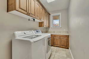 Laundry area with cabinet space, washer and clothes dryer, light tile patterned flooring, and baseboards