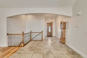 Foyer entrance featuring arched walkways, vaulted ceiling, a chandelier, baseboards, and light tile patterned flooring