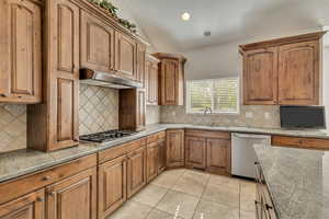 Kitchen with appliances with stainless steel finishes, a sink, under cabinet range hood, lofted ceiling, and light tile patterned flooring