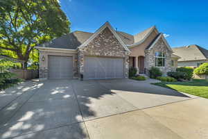 View of front of house featuring an attached garage, driveway, brick siding, stucco siding, and roof with shingles