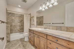 Bathroom with toilet, shower / bath combination with curtain, tile patterned floors, and vanity