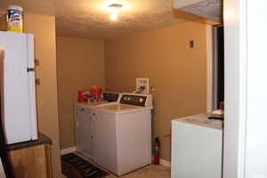 Laundry room with washing machine and clothes dryer, a textured ceiling, and baseboards