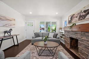 Living area with wood finished floors, ornamental molding, baseboards, a stone fireplace, and recessed lighting