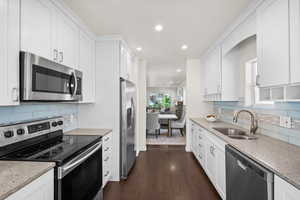 Kitchen with appliances with stainless steel finishes, a sink, recessed lighting, white cabinetry, and dark wood-type flooring