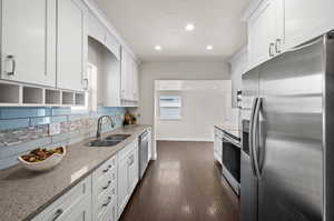 Kitchen featuring appliances with stainless steel finishes, a sink, baseboards, backsplash, and white cabinetry