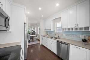 Kitchen featuring stainless steel appliances, a sink, dark wood-style floors, decorative backsplash, and white cabinetry