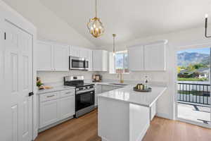 Kitchen with stainless steel appliances, a sink, a peninsula, lofted ceiling, and white cabinetry