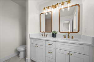 Bathroom with marble finish floors, baseboards, toilet, and double vanity