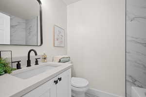 Bathroom featuring marble look tiles, toilet, vanity, and baseboards