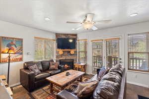 Living room with a textured ceiling, baseboards, a stone fireplace, and a ceiling fan