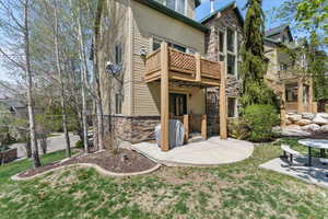 Rear view of house with a patio area, stone siding, and a lawn