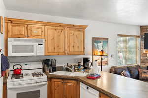 Kitchen featuring a sink, a textured ceiling, white appliances, and dark countertops