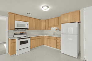 Kitchen with white appliances, a sink, light countertops, light brown cabinetry, and light flooring
