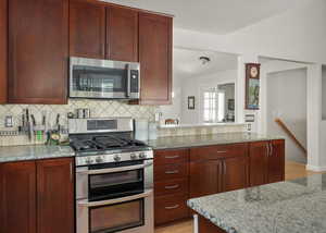 Kitchen with appliances with stainless steel finishes, light wood-style floors, backsplash, and light stone countertops