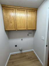Washroom with light wood-type flooring, cabinet space, washer hookup, electric dryer hookup, and a textured ceiling