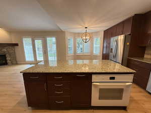 Kitchen featuring dark brown cabinets, white oven, light wood-style floors, and stainless steel refrigerator with ice dispenser