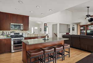 Kitchen featuring stainless steel appliances, decorative backsplash, light wood-style flooring, a kitchen island, and open floor plan