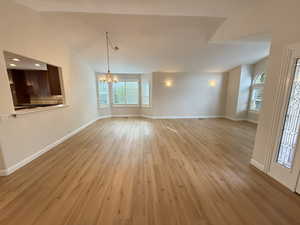 Unfurnished living room with light wood-style floors, a chandelier, and vaulted ceiling