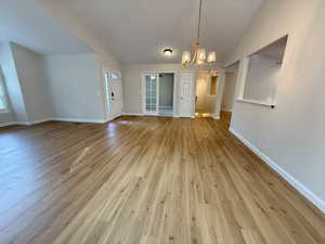 Unfurnished dining area featuring a chandelier, light wood-type flooring, and vaulted ceiling