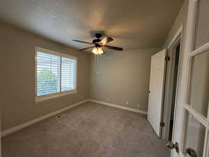 Unfurnished bedroom with light colored carpet, ceiling fan, and a textured ceiling