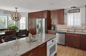 Kitchen featuring appliances with stainless steel finishes, a sink, a chandelier, light stone counters, and tasteful backsplash