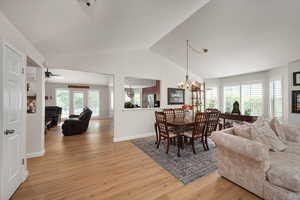 Dining area with light wood-type flooring, a chandelier, lofted ceiling, baseboards, and a ceiling fan