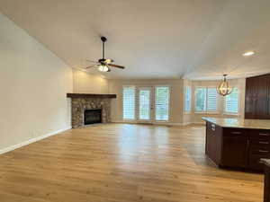 Unfurnished living room featuring light wood finished floors, a fireplace, lofted ceiling, a chandelier, and a ceiling fan
