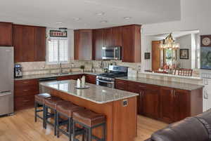 Kitchen featuring appliances with stainless steel finishes, a sink, light wood-style flooring, a kitchen breakfast bar, and a chandelier