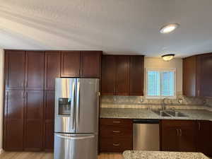 Kitchen featuring appliances with stainless steel finishes, light stone counters, backsplash, light wood-style floors, and a textured ceiling