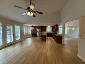 Kitchen featuring a chandelier, open floor plan, dark brown cabinets, a center island, and light wood-style flooring