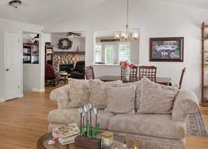 Living area featuring wood finished floors, ceiling fan, lofted ceiling, a chandelier, and a stone fireplace