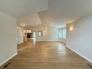 Unfurnished living room featuring a fireplace, vaulted ceiling, light wood finished floors, and a chandelier