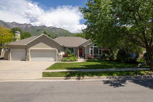 Ranch-style home with a garage, a mountain view, concrete driveway, a front lawn, and stone siding