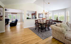 Dining space featuring a chandelier, light wood-style flooring, lofted ceiling, baseboards, and ceiling fan