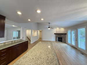 Unfurnished living room with a stone fireplace, light wood-style flooring, recessed lighting, vaulted ceiling, and ceiling fan