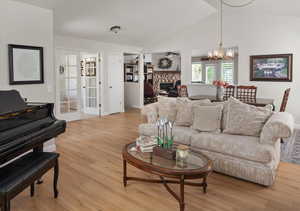 Living area featuring light wood-type flooring, a chandelier, a fireplace, lofted ceiling, and ceiling fan