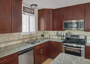 Kitchen featuring appliances with stainless steel finishes, dark brown cabinets, a sink, and light stone counters