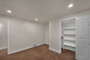 Unfurnished bedroom with dark carpet, a spacious closet, baseboards, recessed lighting, and a closet
