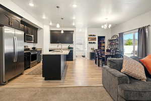 Kitchen featuring appliances with stainless steel finishes, open floor plan, a sink, a chandelier, and an island with sink