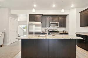 Kitchen featuring appliances with stainless steel finishes, light stone counters, a sink, a kitchen island with sink, and recessed lighting