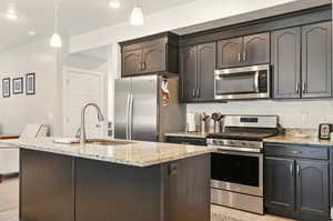 Kitchen with stainless steel appliances, a sink, light stone counters, hanging light fixtures, and recessed lighting