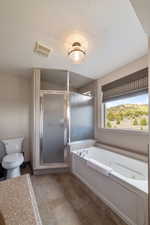 Bathroom featuring a whirlpool tub, a shower stall, toilet, and a textured ceiling